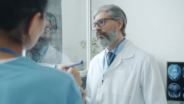 Médico e enfermeiro de uniforme falando olhando para varreduras cerebrais discutindo diagnóstico no hospital — Vídeo de Stock