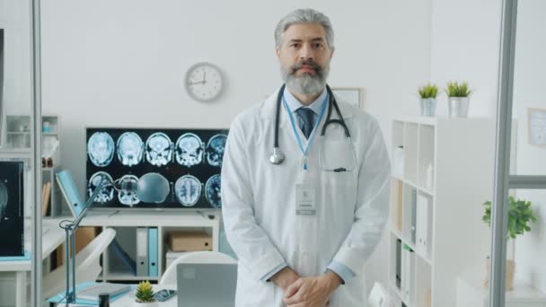 Portret doświadczonego lekarza w białej sukni stojącego w gabinecie kliniki — Wideo stockowe