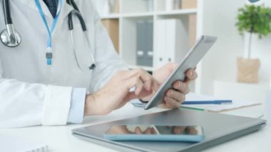 Hastane ofisindeki tablet dokunmatik ekranı kullanarak tıbbi üniformalı bir erkeğin yakın çekimi.