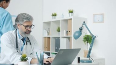 Doktor dizüstü bilgisayar kullanıp modern hastane ofisinde çalışan hemşireyle MRI taramalarını tartışıyor.