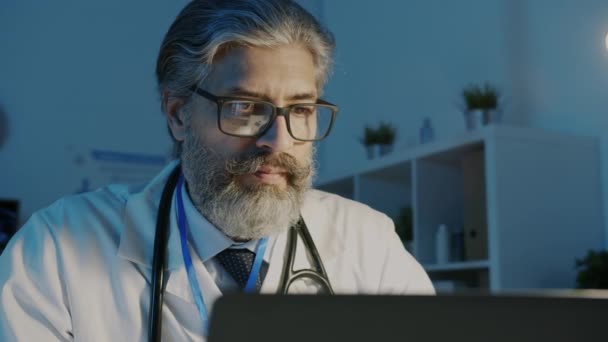 Dojrzały mężczyzna lekarz za pomocą laptopa pracy w nocy i picia wyjąć kawę w pokoju szpitalnym — Wideo stockowe