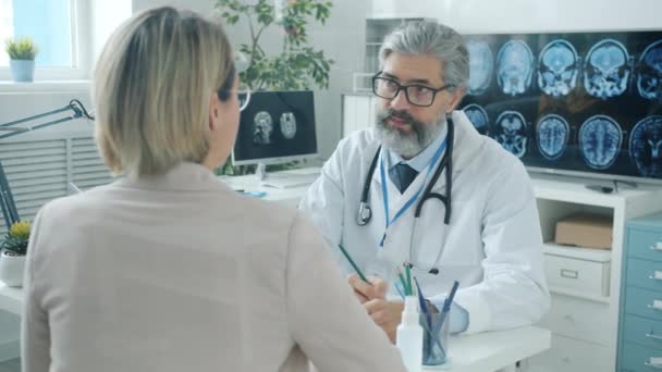 Medical specialist consulting young woman listening to patient taking notes in hospital office — Stock Video