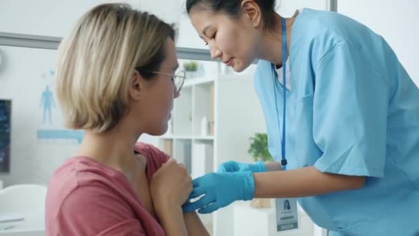 Infirmière en uniforme injectant le vaccin covid-19 à une jeune femme sérieuse dans une chambre d'hôpital — Video