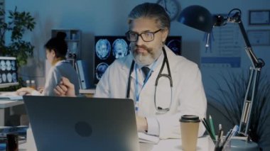 Üniformalı doktorlar akciğer röntgeni üzerinde çalışıyorlar ve geceleri hastanede çalışan bilgisayarları kullanıyorlar.