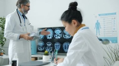Doktorlar MRI beyin taramalarını inceliyor. Konuşuyorlar. Klinikte tıbbi görüşlerini paylaşıyorlar.