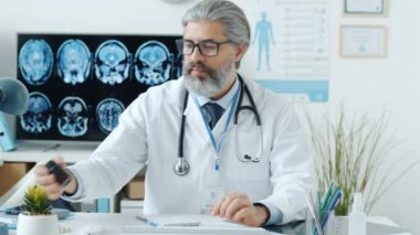 Genel doktor, internette ilaç yazan haplar gösteriyor. Klinikteki kameraya bakıyor.