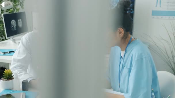 Врач и медсестра за планшетным сенсорным экраном и беседой в больничном кабинете — стоковое видео