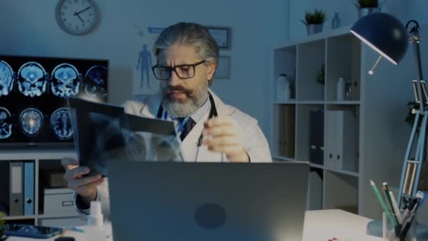 Zmęczony lekarz badający rezonans magnetyczny płuc zdjęcia zdejmujące okulary uczucie wyczerpania w nocy w ciemnym biurze — Wideo stockowe