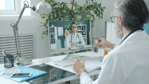 Médecins hommes et femmes discutant de pilules tenant des bouteilles lors d'un appel vidéo en ligne en utilisant PC à l'hôpital — Video