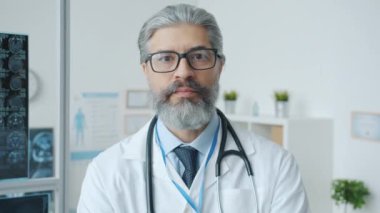 Klinikte duran gözlüklü ve üniformalı deneyimli bir doktorun portresi.