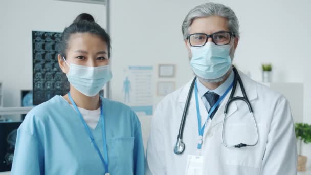 Portrait of doctor and nurse wearing medical masks and uniform standing in office room — Stock Video