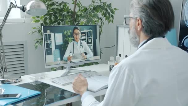 Médico masculino conversando com colega durante videochamada online usando computador no hospital — Vídeo de Stock