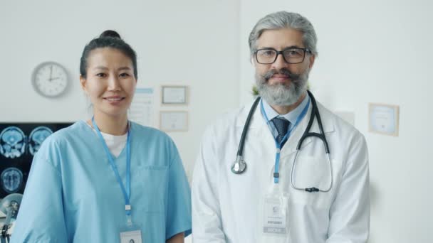 Портрет мужчины и женщины - медперсонал, стоящий в кабинете клиники и улыбающийся, глядя в камеру — стоковое видео