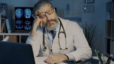 Bitkin düşmüş yetişkin bir doktor uykusunda uyanıyor ve karanlık ofiste geç saatlere kadar çalışan bir dizüstü bilgisayarla uyanıyor.