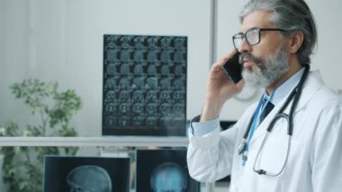 Tıp uzmanı cep telefonuyla modern klinik ofisinde tedaviyi tartışıyor.