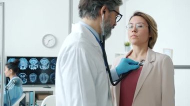 Klinikte kadın hasta muayene ederken erkek doktor steteskop kullanıyor.