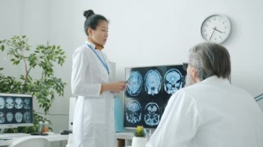 Doktorlar MRI beyin taramalarını tartışıyor. Hastane ofisindeki dijital ekrana işaret ediyorlar.