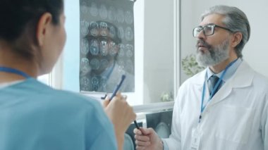 Radyolog asistanıyla konuşuyor. Klinikteki MRI taramalarına bakıyor.