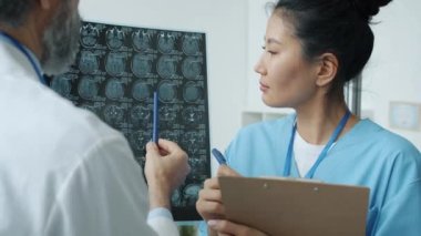 Asyalı hemşire ve Kafkasyalı doktor insan beyin taramasını analiz ediyor ve hastanede tıbbi kayıtlar yazıyor.