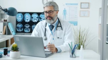 Deneyimli erkek doktor hasta danışmanı. İnternette çalışıyor. Ofisteki bilgisayarı kullanıyor.