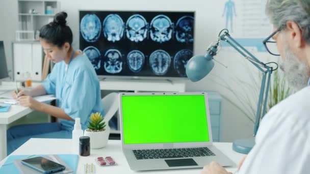 Médico usando la computadora portátil de la pantalla verde de la llave del croma mientras que la enfermera escribe expedientes médicos en hospital — Vídeos de Stock
