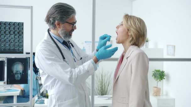 医師への喉の痛みを示す女性患者オープン口のサイドビューで医師に白いガウンで病院オフィス — ストック動画