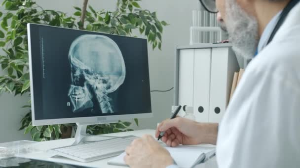 Médico radiólogo analizando imágenes del cráneo humano mirando la pantalla de la computadora y brujeando en el interior del hospital — Vídeo de stock