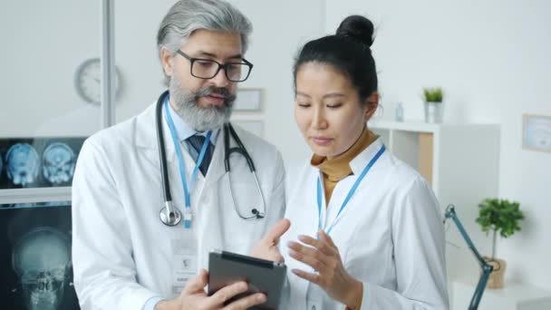 사무실에 서 있는 태블릿 화면을 보면서 의학적 인 문제에 대해 이야기하고 있는 남녀 의사들 — 비디오