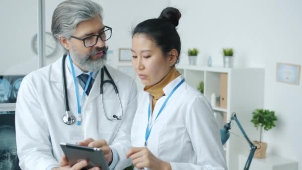 Dokter pria Kaukasia dan wanita Asia berbicara dan melihat layar laptop di kantor rumah sakit — Stok Video