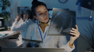 Radyolog, tıp üniformalı Asyalı kadın geceleri karanlık ofiste çalışan akciğer tomografisi çalışıyor.