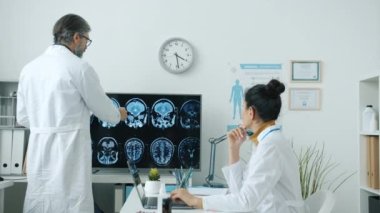 Doktorlar erkek ve kadın beyin taramalarını analiz ediyor ve hastane odasında hastalıkları tartışıyor.