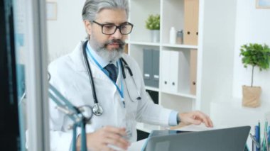 Ofisteki dizüstü bilgisayarı kullanarak online video konsültasyonu sırasında MRI taramasını tartışan olgun bir doktor