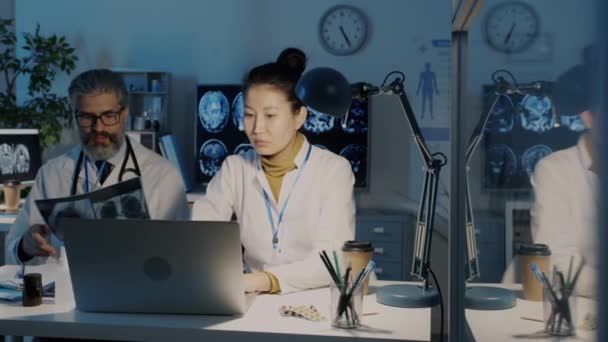 Médico experiente consultando jovem colega discutindo exames pulmonares de RM no escritório à noite — Vídeo de Stock