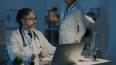 Kadın doktor, erkek meslektaşına kahve getiriyor. Gece karanlık ofiste birlikte çalışıyoruz.