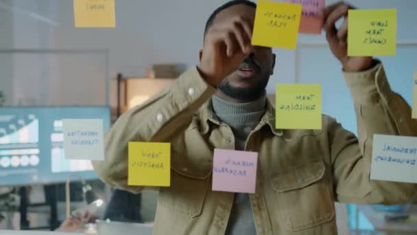 African American businessman working with sticky notes in dark office at night — Stock Video