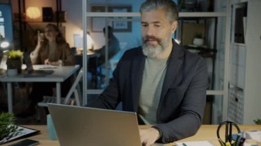Yetişkin iş adamının portresi. Laptop kullanıyor ve akşamları karanlık ofiste kahve içiyor.