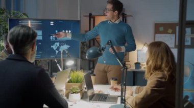 İşadamı, karanlık ofiste dijital ekranla iş arkadaşlarıyla konuşma yaparak sunum yapıyor.