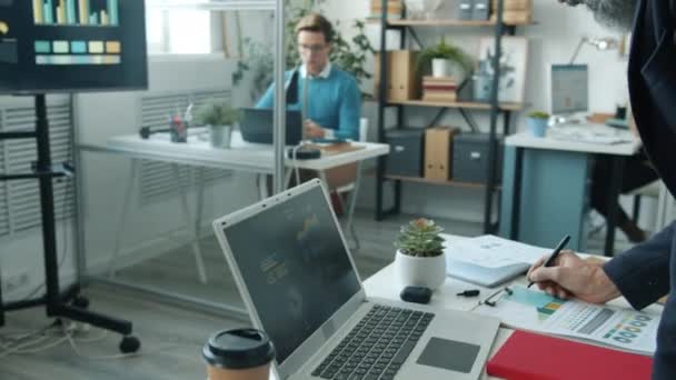 Retrato de homem de negócios trabalhando com laptop no escritório moderno, enquanto os colegas estão ocupados com o trabalho — Vídeo de Stock