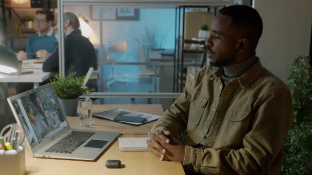 Uomo d'affari afro-americano che ha un incontro online con una collega donna usando un computer portatile in un ufficio buio — Video Stock