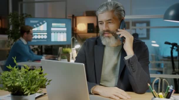 Framgångsrik anställd talar på mobiltelefon diskuterar företag som arbetar på kontoret på natten — Stockvideo