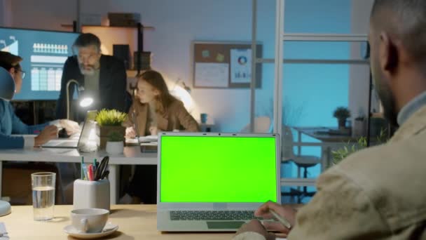 Afro-Amerikaanse kantoormedewerker met behulp van laptop met chroma sleutel groen scherm op de werkplek 's nachts — Stockvideo