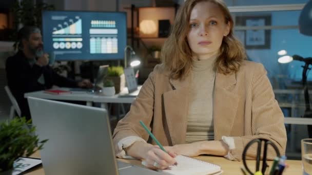 Portrait au ralenti d'une femme d'affaires assise à table dans un lieu de travail sombre et regardant la caméra — Video