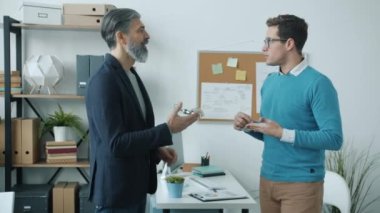 İşadamları konuşurken ve el sıkışırken çalışanlar cam duvar odasındaki masalarda dizüstü bilgisayarlarla çalışıyor.