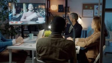 Çevrimiçi video görüşmesi sırasında karanlık ofiste iş tartışan çeşitli iş adamları grubu