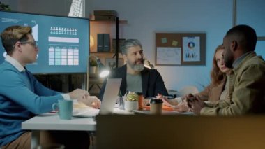 Şirket ekibi karanlık ofiste geç saatlerde iş paylaşımı hakkında konuşuyor.