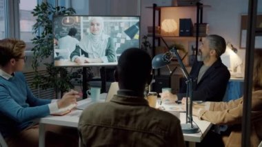 Karanlık ofisteki çevrimiçi toplantı sırasında Müslüman iş ortağıyla konuşan çeşitli çalışanlar.