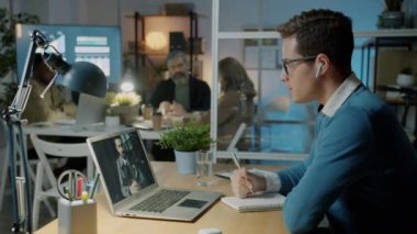 İş adamları geceleri ofiste bilgisayar ve kablosuz kulaklık kullanarak iş görüşmesi yapıyorlar.