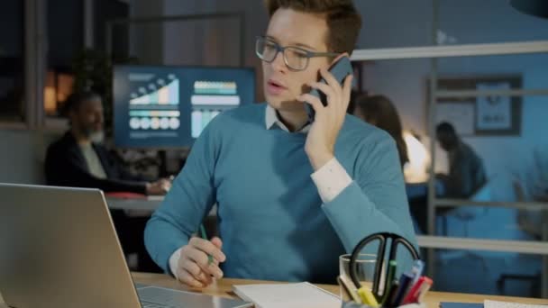 Porträt eines ehrgeizigen Geschäftsmannes, der mit dem Handy telefoniert und im Büro Laptop benutzt — Stockvideo