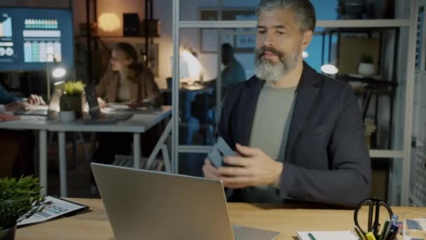 Kontorsarbetare skriva med bärbar dator sedan ringa på mobiltelefon arbetar på kvällen på arbetsplatsen — Stockvideo