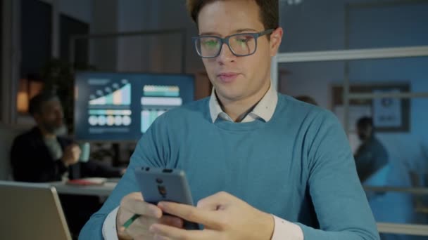 Ritratto di uomo d'affari di successo con smartphone che scrive e sorride lavorando di notte in ufficio — Video Stock